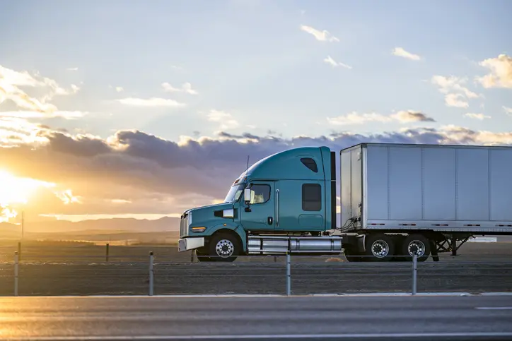 Industrial long hauler big rig green semi truck tractor with chrome parts transporting commercial cargo in loaded dry van semi trailer running on the highway road at sunset time in Connecticut