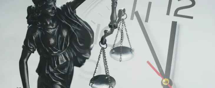 Silver statuette of Justice holding the scales of justice and law enforcement in front of a clock dial in a close up conceptual composite image